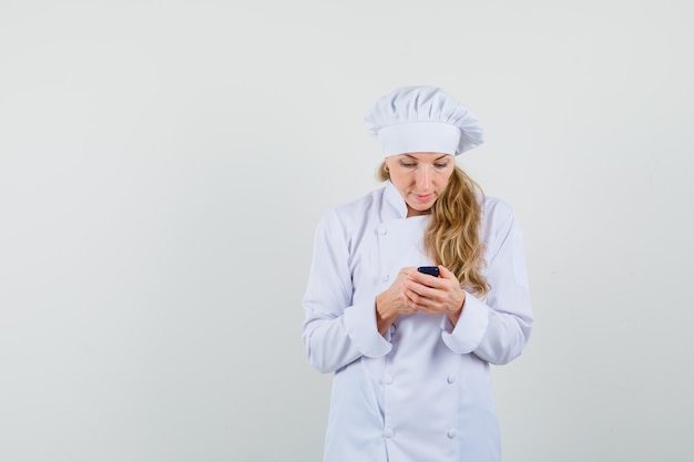 Female chef in white uniform using cellphone and looking busy 