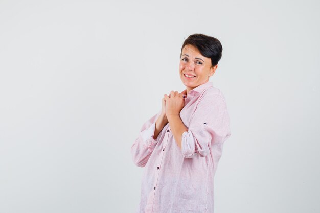 Female clasping hands on chest in pink shirt and looking cute. front view.