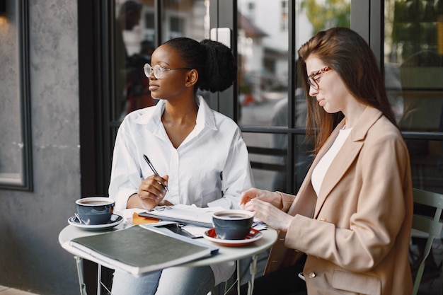 屋外のカフェでデータについて話し合う女性の同僚。ストリートカフェのドキュメントを使用してビジネスプロジェクトの生産戦略を分析する多民族の女性