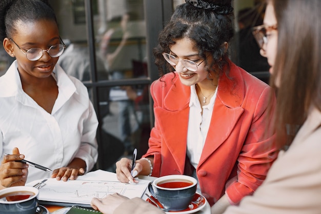 카페 야외에서 데이터를 논의하는 여성 동료. 거리 카페에서 문서를 사용하여 비즈니스 프로젝션을위한 생산적 전략을 분석하는 다인종 여성 명