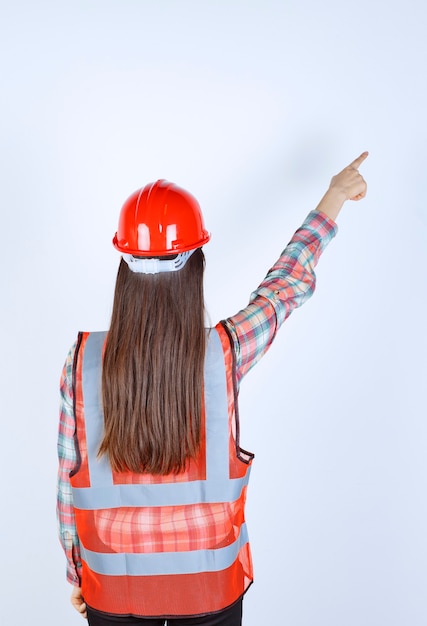 Free photo female construction engineer in red helmet and safety mask pointing ahead.