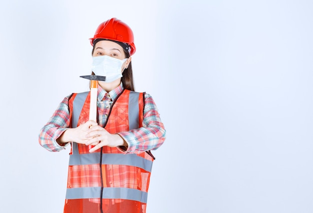 Free photo female construction engineer in safety mask and red helmet holding a wooden handled ax.