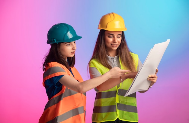 Free photo female construction engineers working together and discussing the project plan on colorful background.