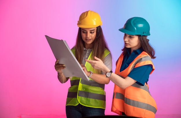 Female construction engineers working together and discussing the project plan on colorful wall.