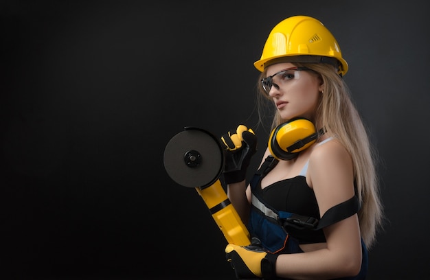 The female construction worker in a hard hat with angle grinder over black background