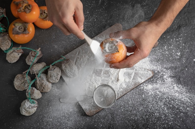 Female cook adds flour to sweet persimmon in kitchen