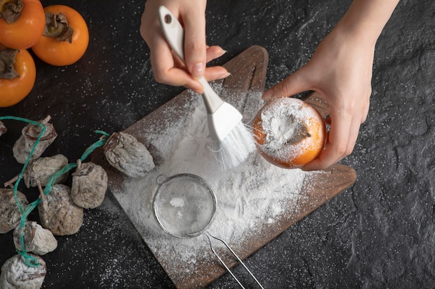 Free photo female cook decorating persimmon with flour on black surface