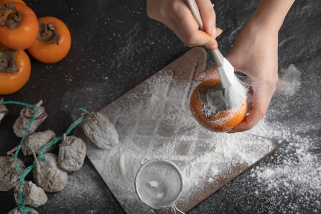 Female cook decorating persimmon with flour on black surface