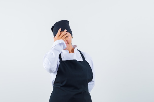 Free photo female cook holding hand on face in uniform, apron and looking happy. front view.