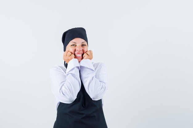 制服、エプロン、興奮して頬に手をつないでいる女性料理人。正面図。