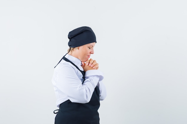 制服、エプロンで握りしめられ、夢のように見える手をつないでいる女性料理人。正面図。