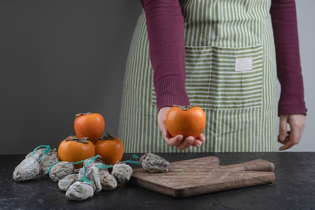 Female cook holding single persimmon fruit on black table