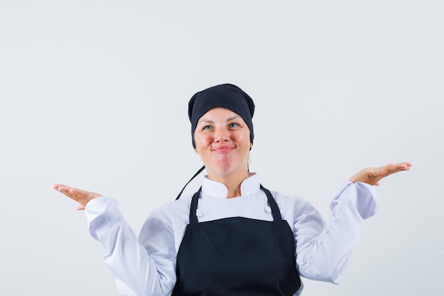 Foto gratuita cuoco femminile che fa gesto di scale in uniforme, grembiule e sguardo allegro. vista frontale.