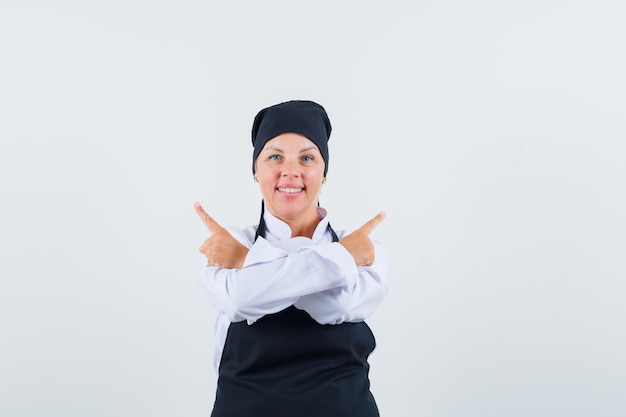 Female cook pointing away in uniform, apron and looking confident. front view.