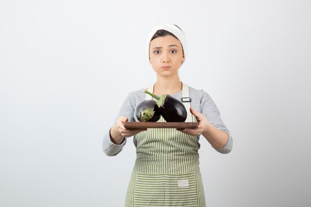 Free photo female cook posing with plate of big eggplants on white.