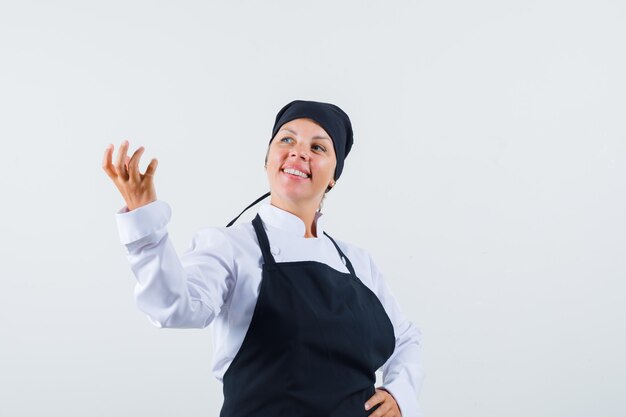 Female cook pretending to hold something in uniform, apron and looking cheerful. front view.