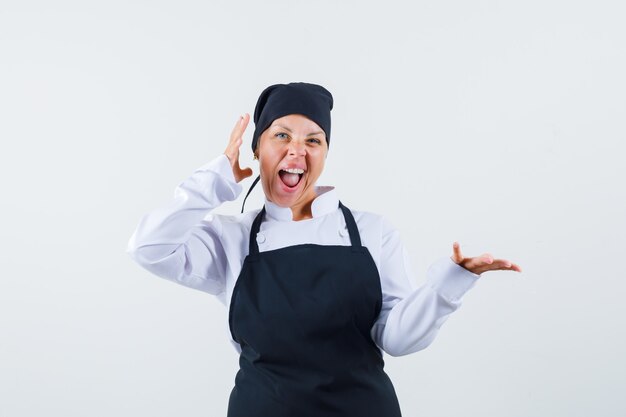 Female cook pretending to hold something in uniform, apron and looking happy , front view.