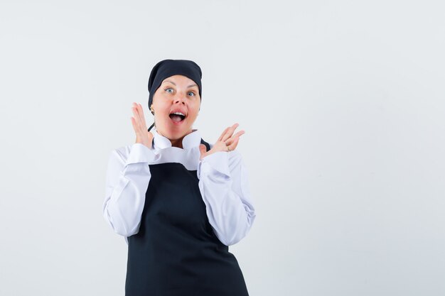 Female cook raising hands in uniform, apron and looking excited. front view.