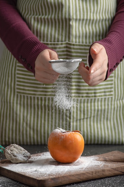 Free photo female cook spilling flour to sweet persimmon in kitchen