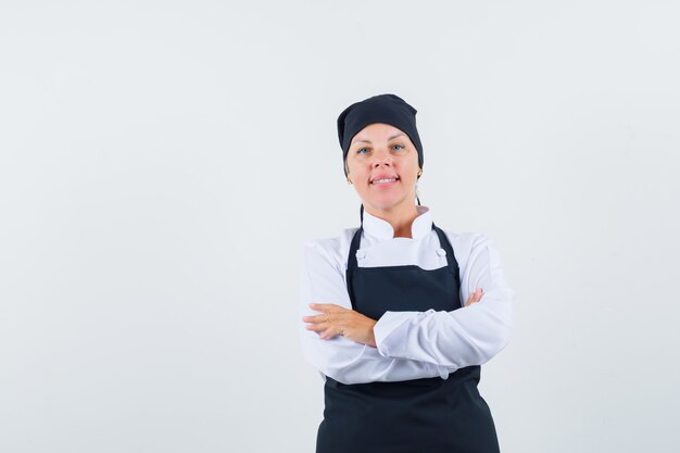 制服、エプロン、自信を持って腕を組んで立っている女性料理人。正面図。