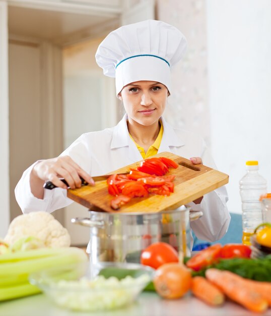 Женский повар в toque работает на коммерческой кухне