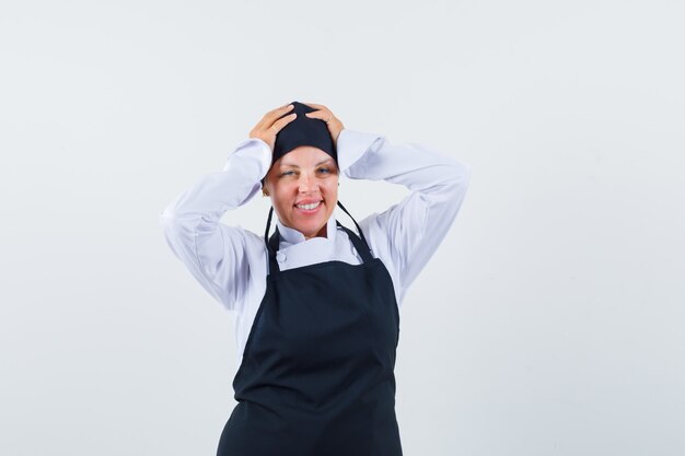 Female cook in uniform, apron holding hands on head and looking joyful , front view.