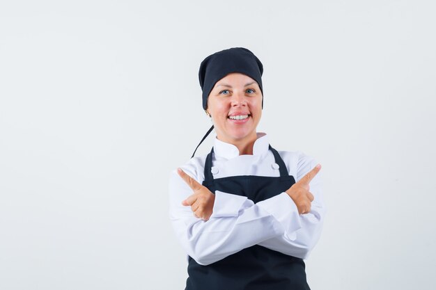 Female cook in uniform, apron pointing away and looking cheerful , front view.