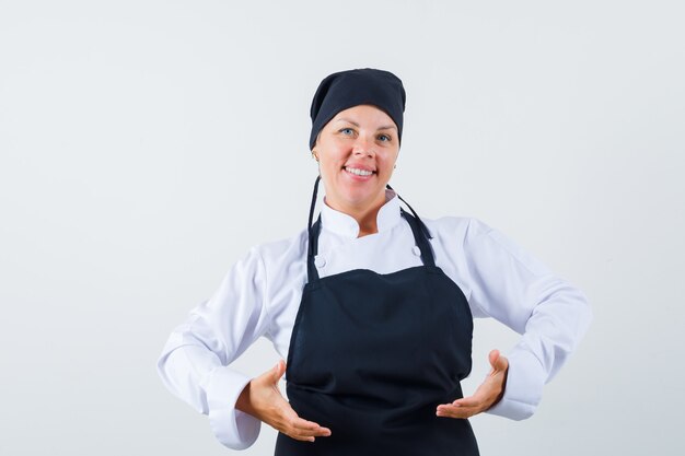 Female cook in uniform, apron pretending to raise or hold something and looking confident , front view.