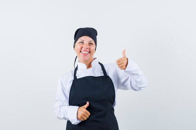 Female cook in uniform, apron showing double thumbs up and looking glad , front view.