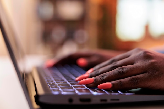 Женщина-копирайтер печатает сообщение на клавиатуре ноутбука, крупным планом на ухоженных ногтях. Молодой афро-американский SMM-менеджер просматривает интернет, пишет электронную почту на компьютере, фокусируется на руках