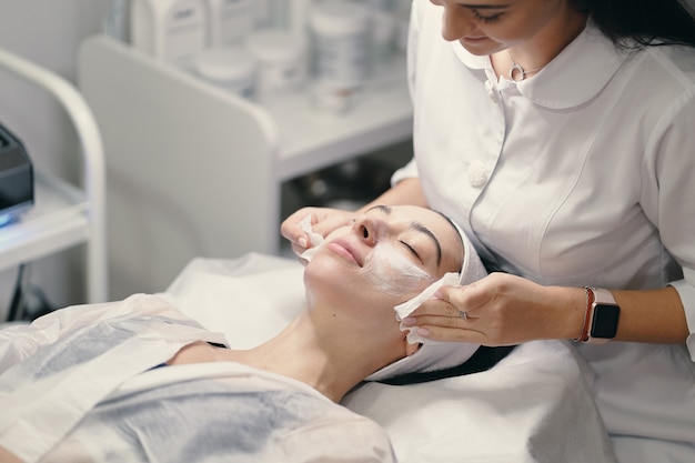 Female cosmetologist making facial treatment to a beautiful woma