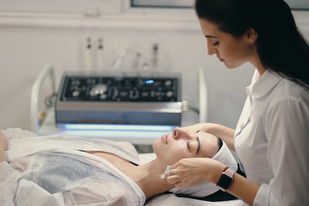 Female cosmetologist making facial treatment to a beautiful woma