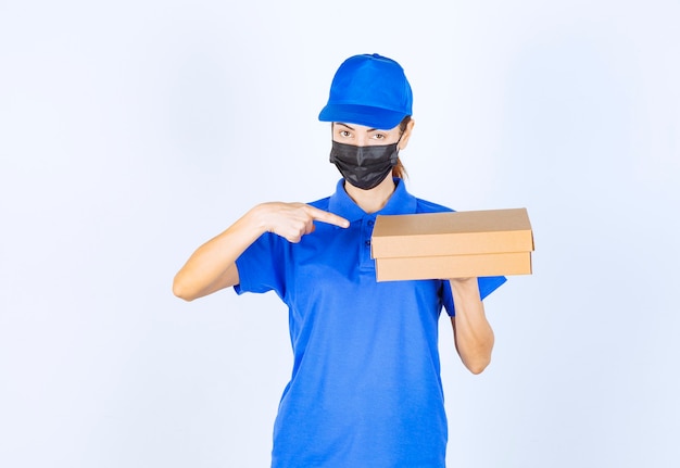 Female courier in blue uniform and face mask delivering a cardboard box to the customer. 