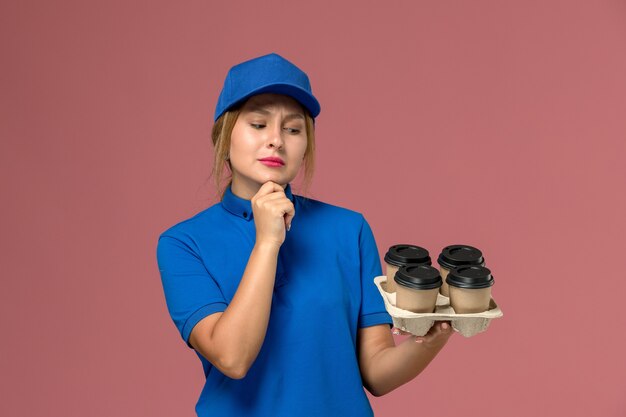 ピンクのコーヒーの茶色の配達カップを保持している青い制服を着た女性の宅配便、サービスワーカーの制服配達
