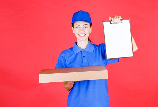 Female courier in blue uniform holding a cardboard takeaway pizza box and presenting the signature list . 