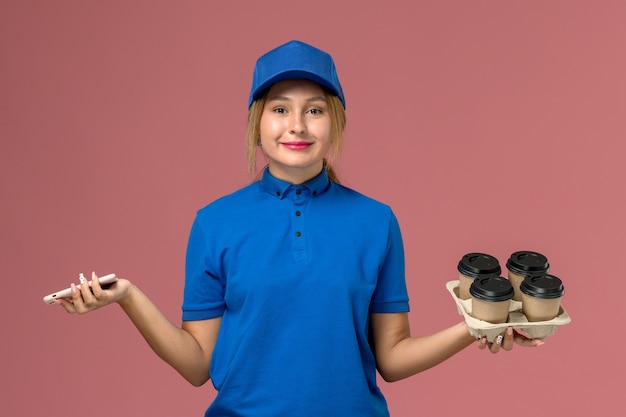 전화를 들고 파란색 유니폼을 입은 여성 택배와 밝은 분홍색, 서비스 유니폼 배달 작업에 갈색 컵 커피