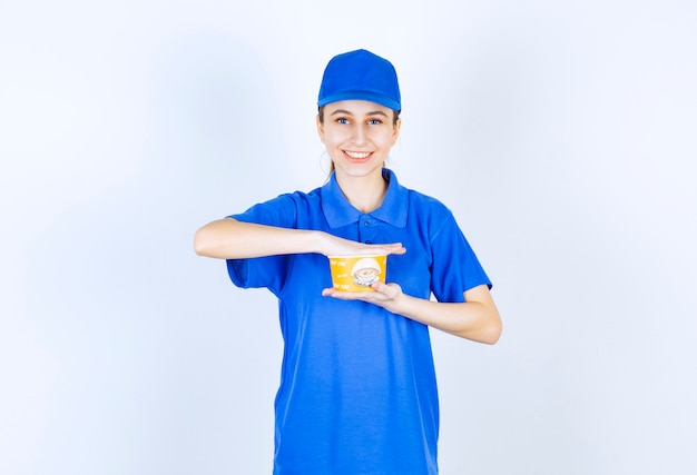 Female courier in blue uniform holding a takeaway noodle cup.