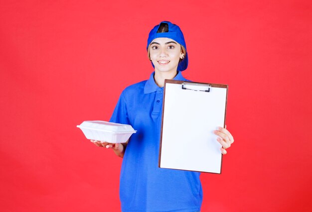 Женский курьер в синей форме держит белую коробку для еды и представляет контрольный список на подпись