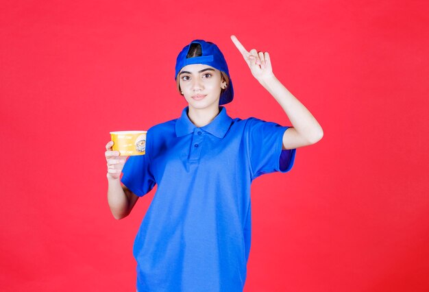 Female courier in blue uniform holding a yellow noodles cup and has a good idea. 