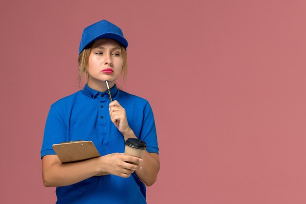 female courier in blue uniform posing holding cup of coffee and notepad thinking on pink, service uniform delivery girl