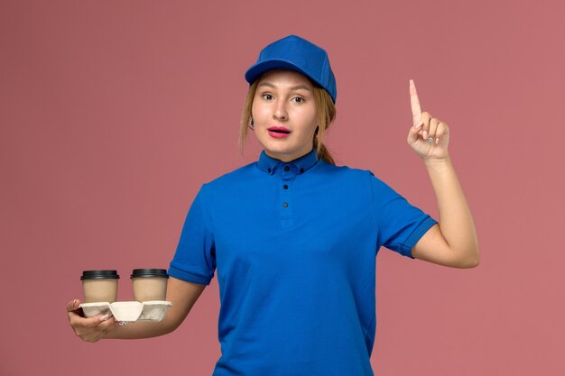 파란색 유니폼 포즈와 핑크, 서비스 유니폼 배달 작업에 제기 손가락으로 커피 잔을 들고 여성 택배