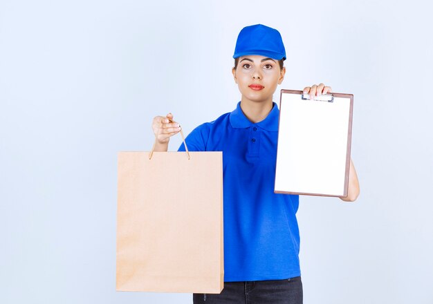 Female courier carrying paper craft bag and showing clipboard.