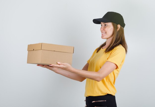 Female courier delivering cardboard box in t-shirt, pants and cap