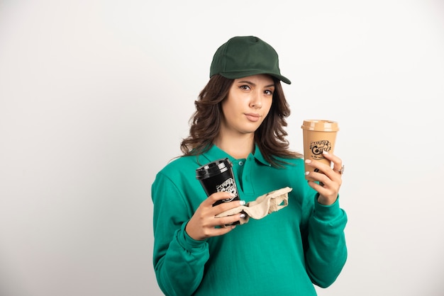 Female courier in green uniform holding coffee cups with serious expression.