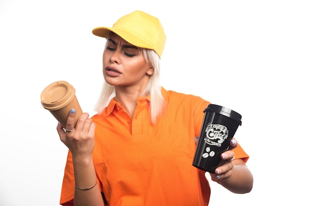 Female courier holding and looking at two cups of coffees on white background. High quality photo