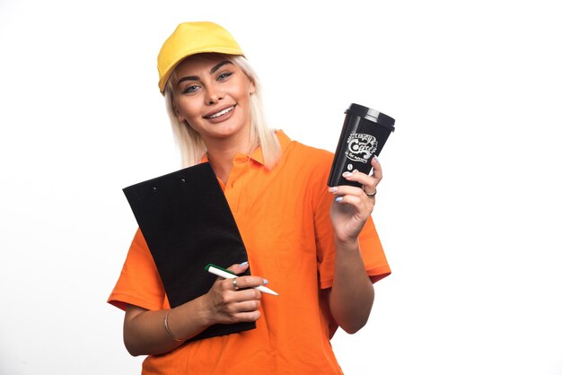 Female courier holding notebook and giving away a cup of coffee on white background. High quality photo