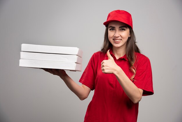 Female courier holding pizza boxes and giving thumbs up. 