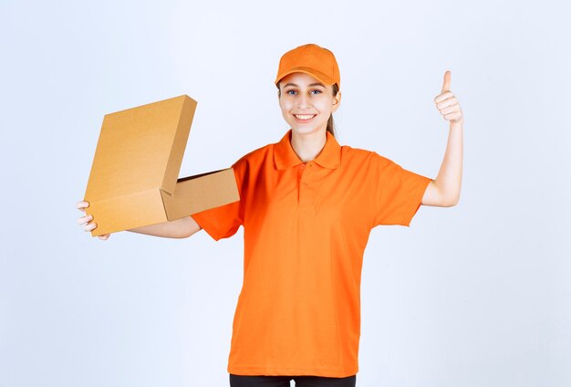 無料写真 開いた段ボール箱を保持し、肯定的な手のサインを示すオレンジ色の制服を着た女性の宅配便。