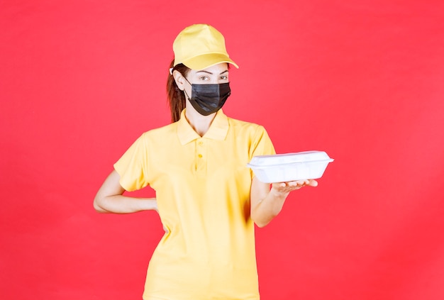 テイクアウトパッケージを保持している黄色の制服と黒のマスクの女性の宅配便