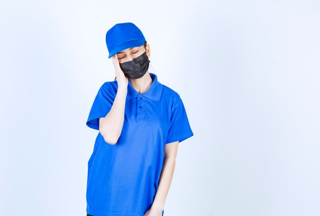 Female courier in mask and blue uniform looks sleepy and tired.